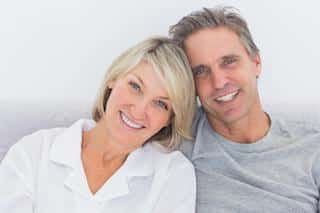 Two smiling adults posing together against a white background for a dental care practice portrait.