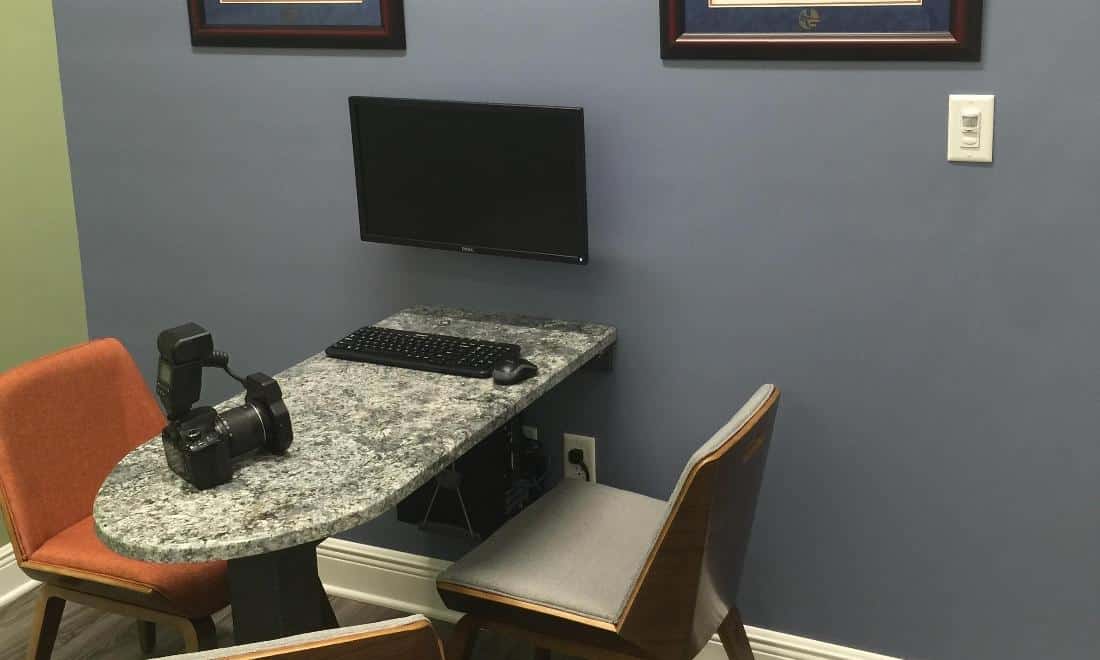Modern dental office workspace with computer monitor, orange chair, and granite countertop desk.