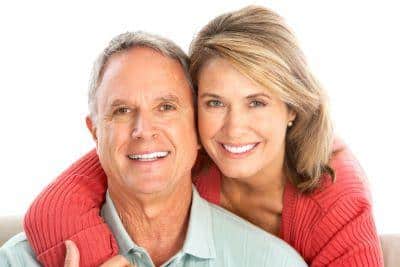 Smiling mature couple in casual red and white clothing against white background, dental care portrait.