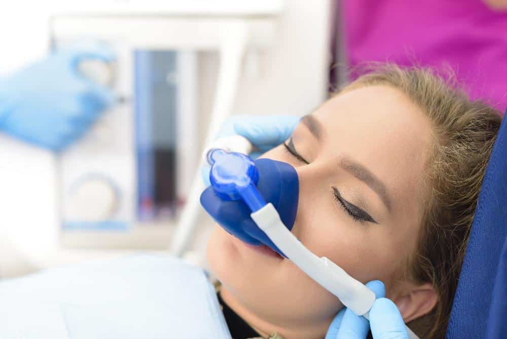 Patient receiving dental examination with blue protective mask in dental office setting.