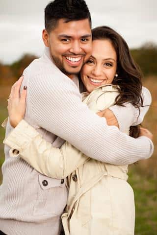 Smiling couple embracing outdoors in casual autumn clothing, natural field setting.