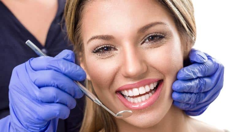 Smiling woman receiving dental examination from dentist wearing blue gloves in dental office.