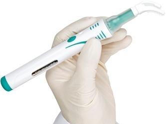 Gloved hand holding electronic dental handpiece instrument against white background.