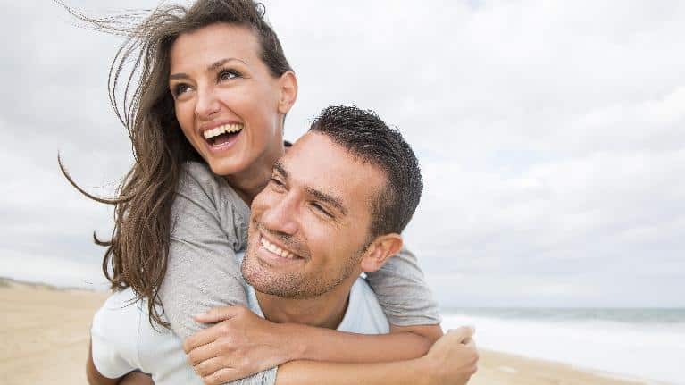 Happy couple embracing on beach with ocean and sky in background.