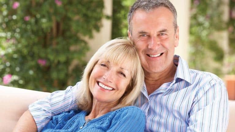 Happy middle-aged couple smiling outdoors with greenery in background