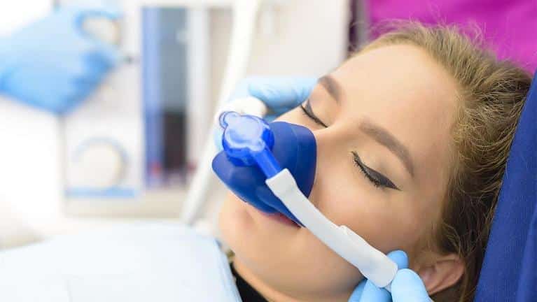 Patient receiving dental treatment with blue protective mask and equipment in dental office setting.