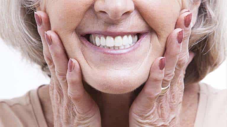 Woman smiling brightly while holding her face, showcasing healthy teeth and skin care.