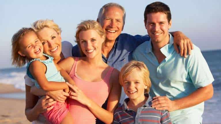 Happy family of six smiling together on a sunny beach in casual clothing.