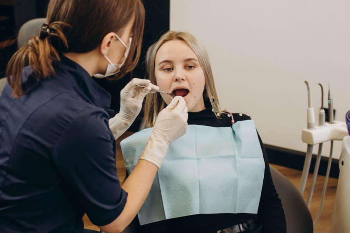 Dental hygienist examining patient's teeth in professional clinic setting with dental bib.
