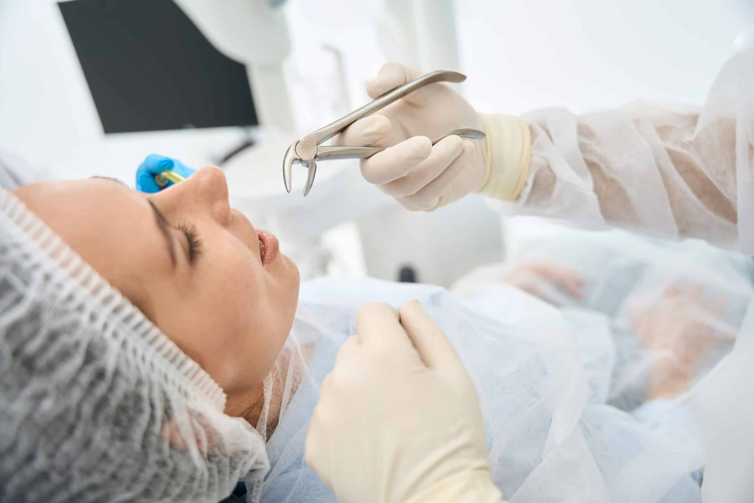 Dentist in gloves holding instruments performing oral examination on patient in dental office.